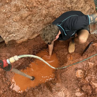 D&R plumber working in a red-dirt excavation, sealing a burst water pipe