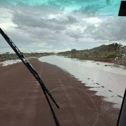 View through a service vehicle windscreen onto a flooded outback red-dirt road